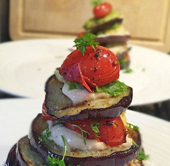 Una colorida torre de berenjena a la parrilla con aguacate, hummus y tomatitos